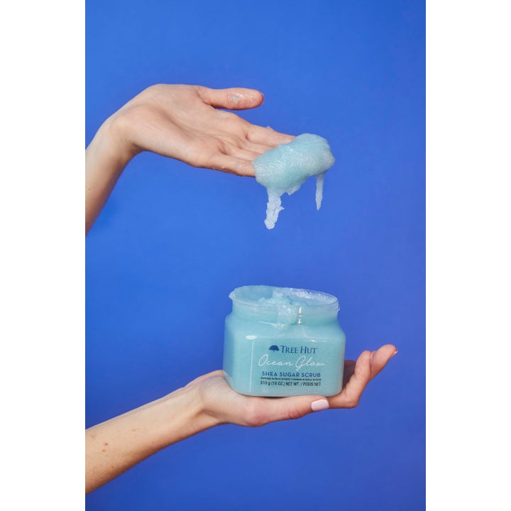 Tree Hut Shea Sugar Scrub Ocean Glow 510 g eksfolierende kroppsskrubb med blå tekstur som drypper fra en hånd.