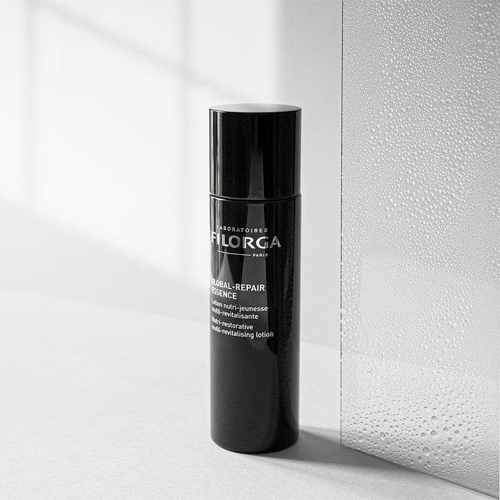 Filorga Global-Repair Essence 150 ml revitaliserende ansiktsvann i svart flaske ved siden av glass