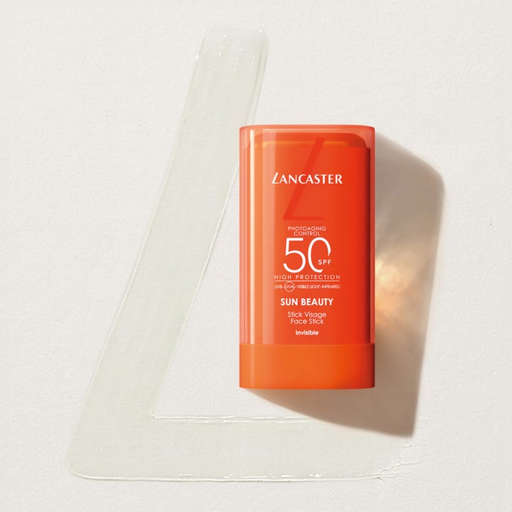 Lancaster Sun Beauty Face Stick 20 g solkrem med SPF 50 over et gjennomsiktig produktstrøk formet som en L.