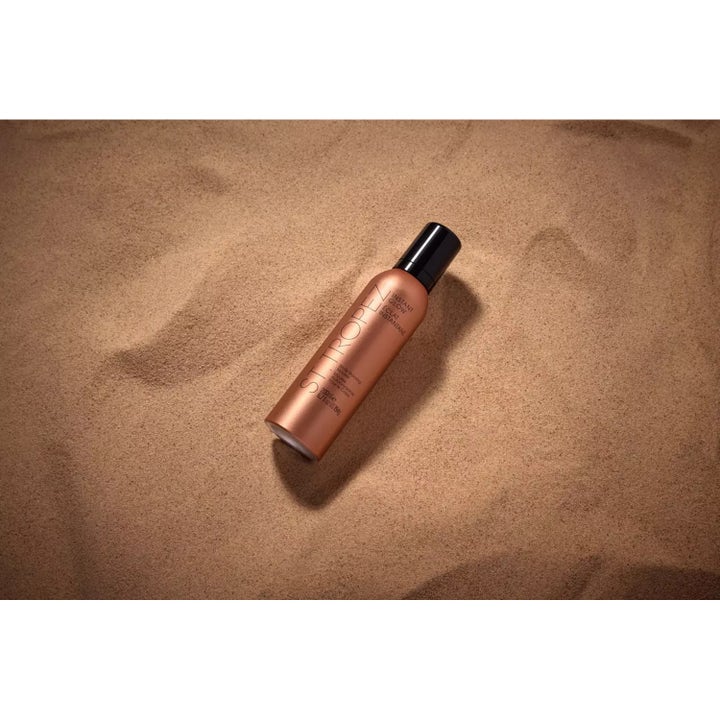 St.Tropez Instant Glow Body Bronzing Mousse 200 ml gir solkysset hud i bronsefarget flaske på sand