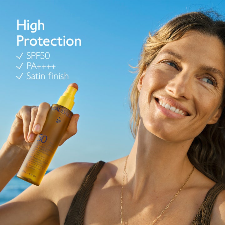 Caudalie Vinosun High Protection Glow Oil SPF50 150 ml sololje på sprayflaske holdt av kvinne i solskinn