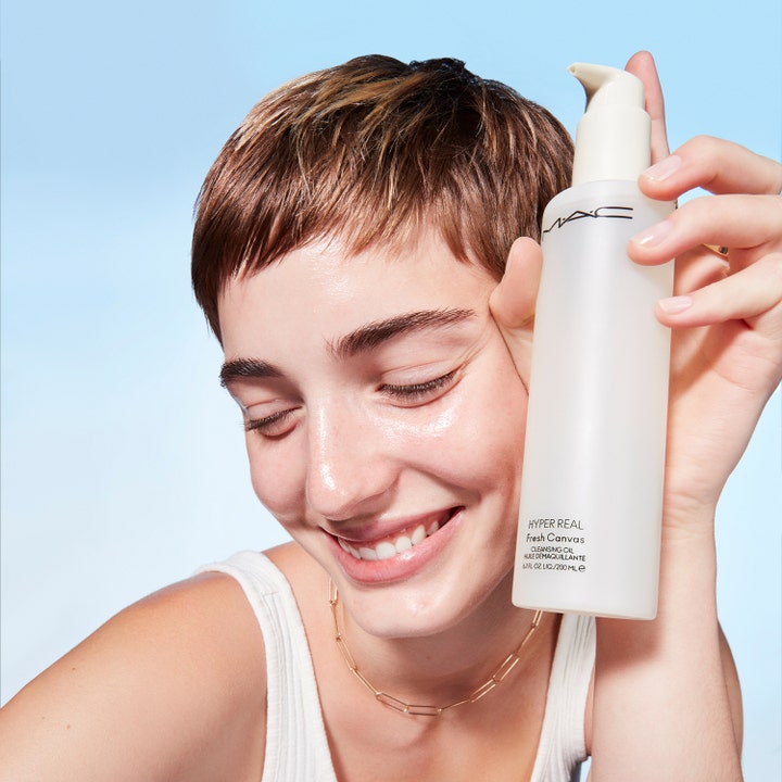 MAC Cosmetics Hyper Real Fresh Canvas Cleansing Oil 200 ml ansiktsrengjøring i hvit pumpeflaske holdt av smilende person