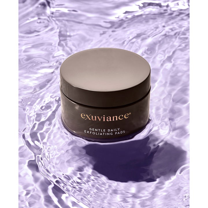 Exuviance Gentle Daily Exfoliating 60 Pads 55 ml exfolierende peeling i en mørk krukke omgitt av lilla vann