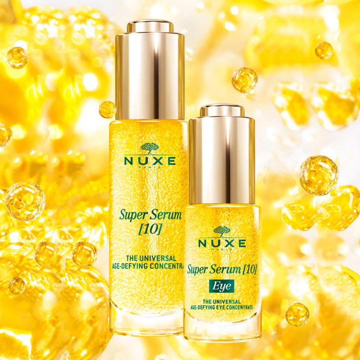Nuxe Super Serum [10] Eye 15 ml anti-aging øyeserum i gullflaske foran en glitrende bakgrunn av gylne bobler.