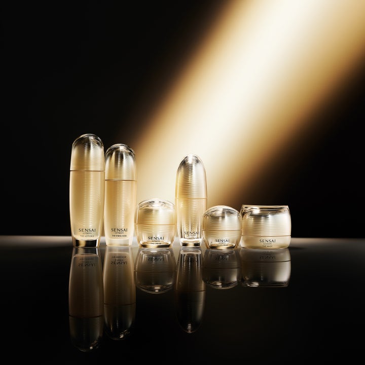 Sensai Ultimate The Concentrate N 30 ml serum i en samling av elegante gullflasker med dramatisk lys og refleksjon.