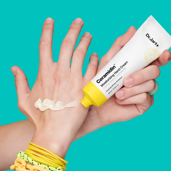 Dr.Jart+ Ceramidin Moisturizing Hand Cream 100 ml fuktighetsgivende håndkrem i hvit tube påføres hånd mot blå bakgrunn.