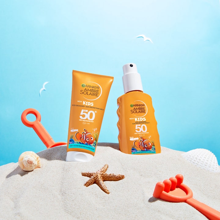 Garnier Ambre Solaire Kids 150 ml solkrem SPF 50 i oransje flasker med Nemo-motiv på stranden med sandleker og sjøstjerne.