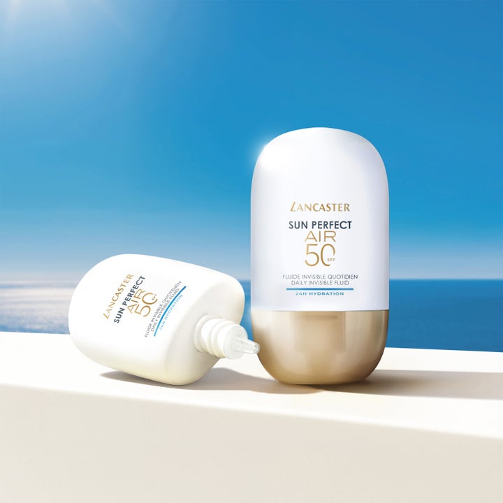 Lancaster Sun Perfect AIR Daily Invisible Fluid 40 ml SPF50 solkrem i hvite flasker med gullbase mot blått hav.