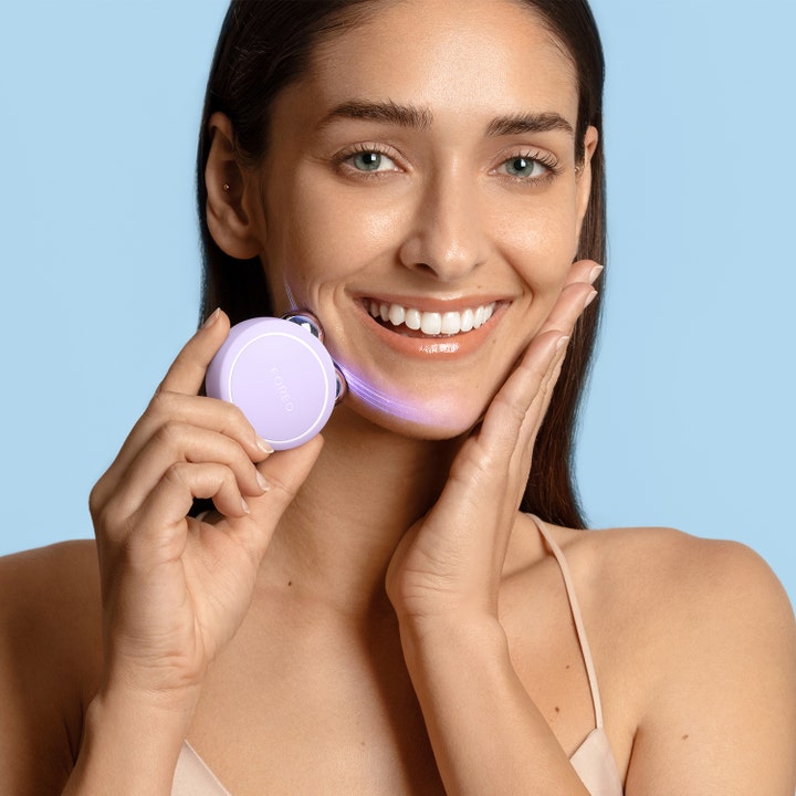 FOREO BEAR 2 go Lavender 1 stk ansiktsløft med mikrostrøm vist på smilende kvinne med lilla lysstråler