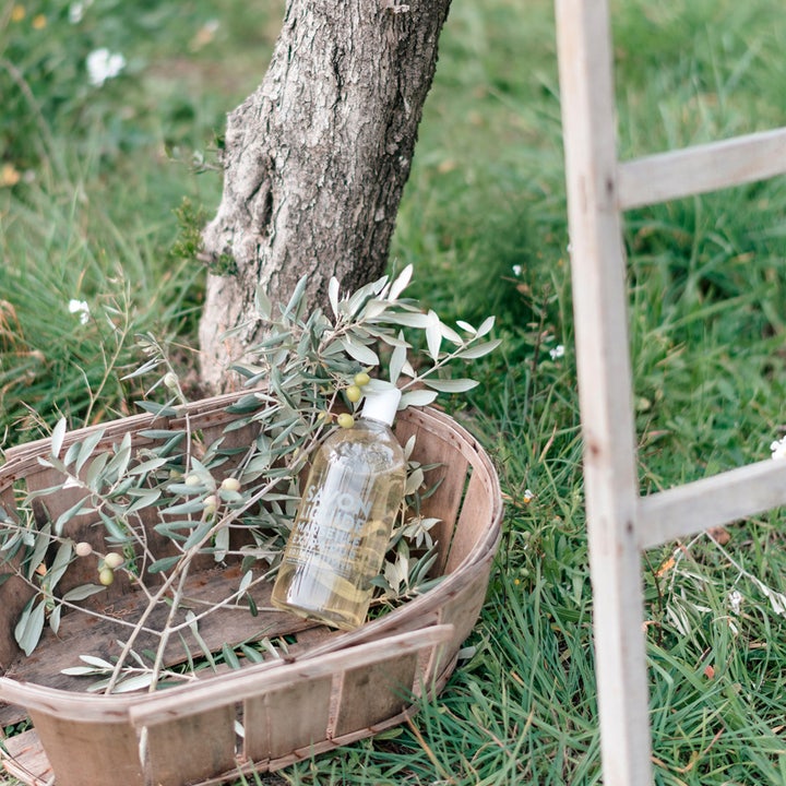 Compagnie de Provence Olive Wood 1000 ml flytende såpe i klar flaske plassert i en trekorg med olivenkvister