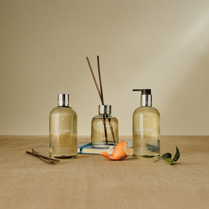 Molton Brown Orange & Bergamot 300 ml oppfriskende håndsåpe i et stilleben med duftpinner og appelsinskall.