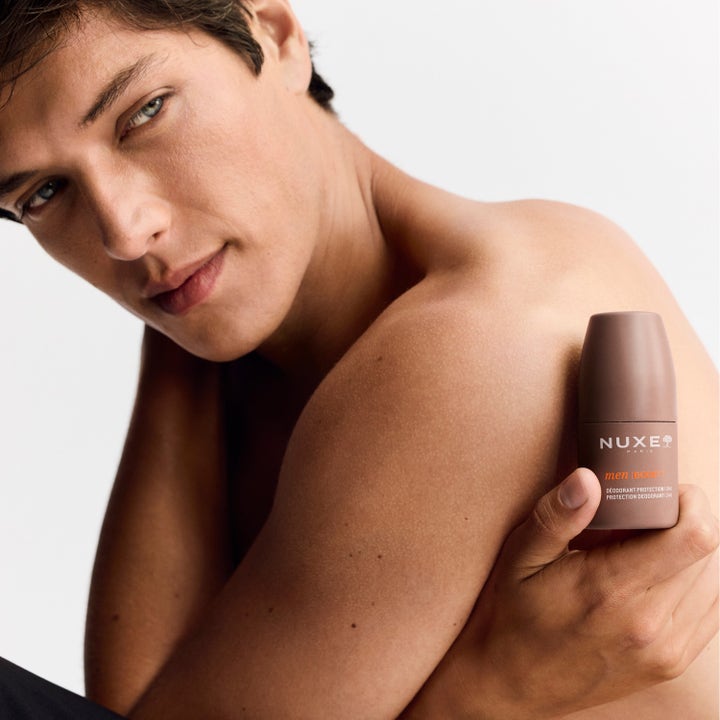 Nuxe Men 24Hr Protect Deo 50 ml i brun hylse holdt av en mann for effektiv beskyttelse mot svette.