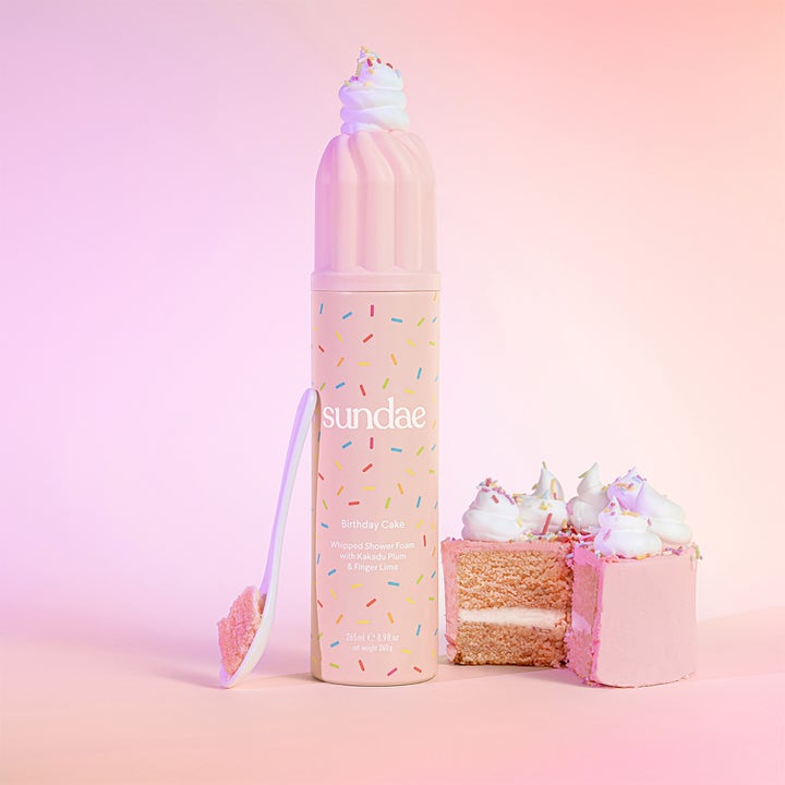 Sundae Whipped Shower Foam Birthday Cake 265 ml pleiende dusjsåpe i rosa boks med strøssel ved siden av en kake