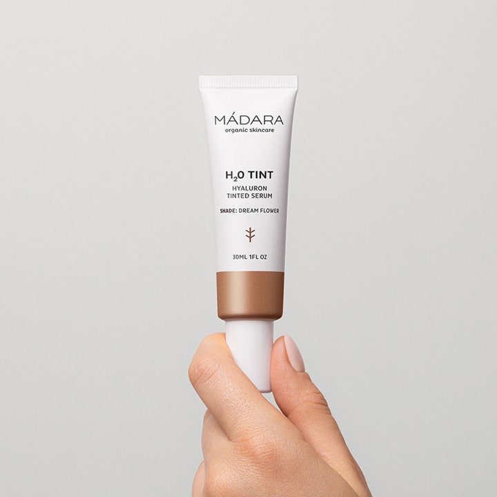 MÁDARA H2O Tint Hyaluron Tinted Serum 30 ml fuktighetsgivende serum i hvit tube som holdes av en hånd