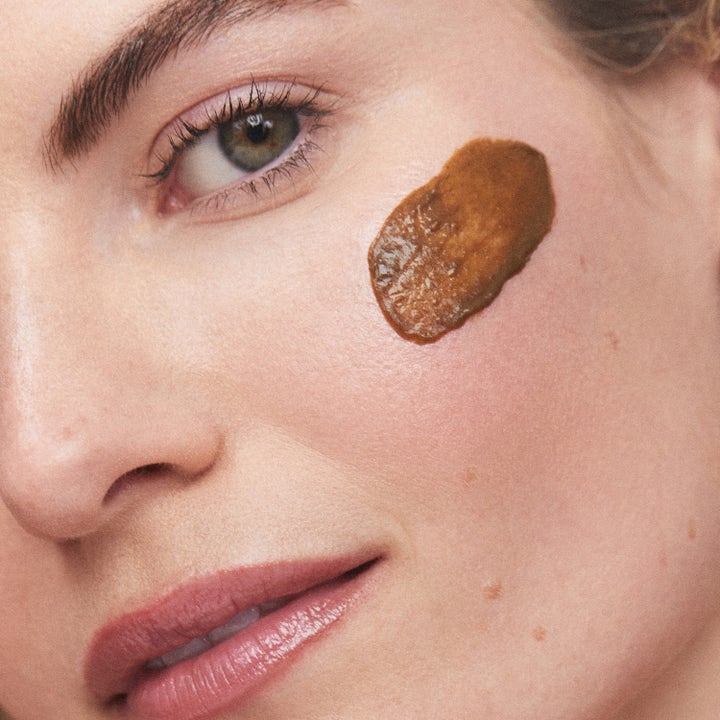 KORA Organics Turmeric Brightening & Exfoliating Scrub & Mask 100 ml ansiktsskrubb med brun kornete tekstur på huden