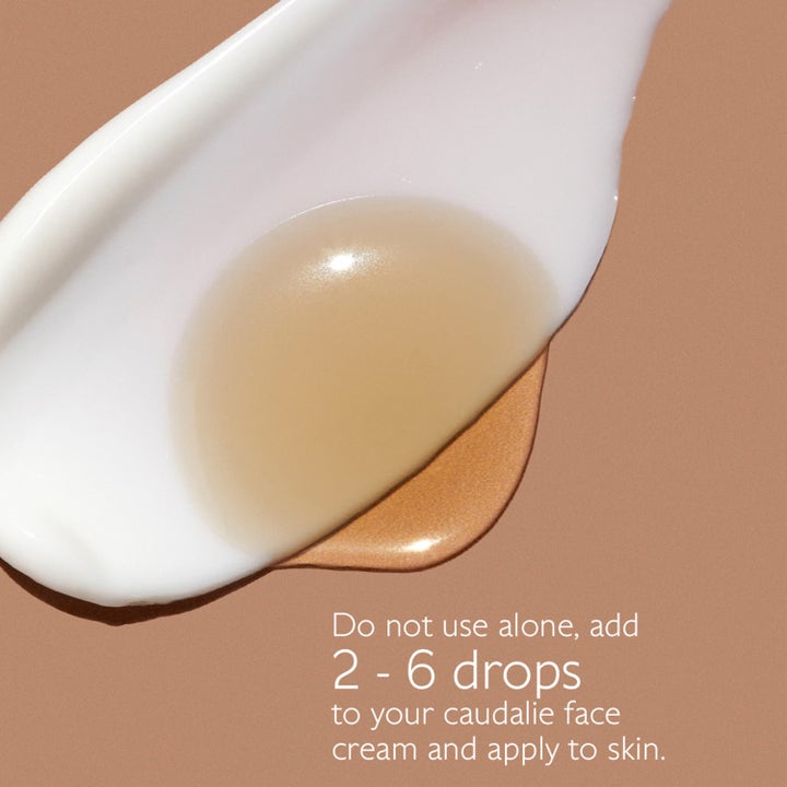 Caudalie Self-Tan Sun Drops 15 ml tanning drops vist som en gyllen dråpe i hvit ansiktskrem på brun bakgrunn