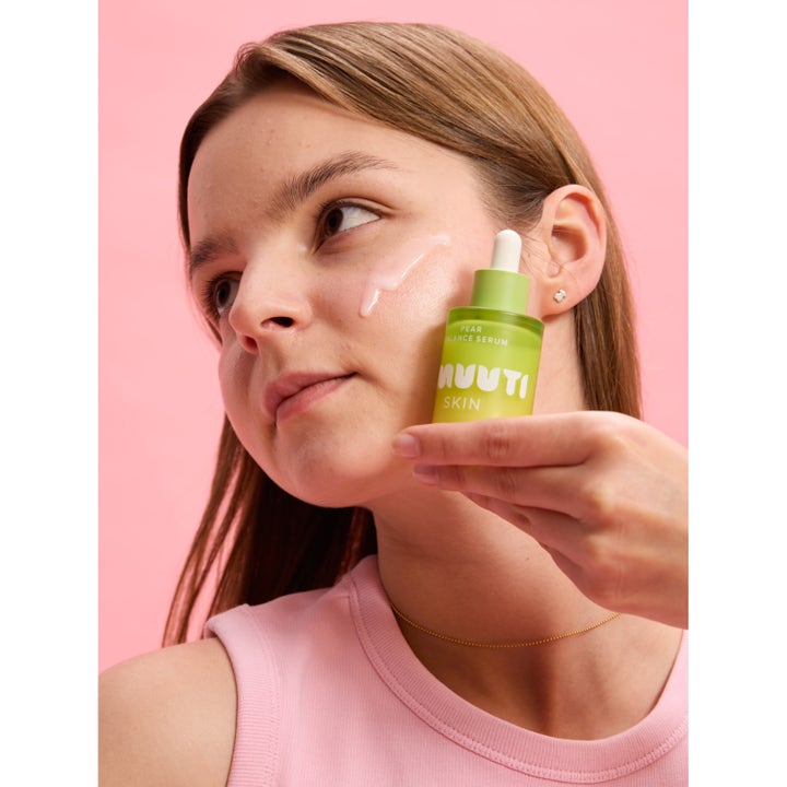 Smuuti Skin Pear Balance Serum 30 ml balanserende serum i grønn glassflaske holdt mot ansikt med rosa dråpe.