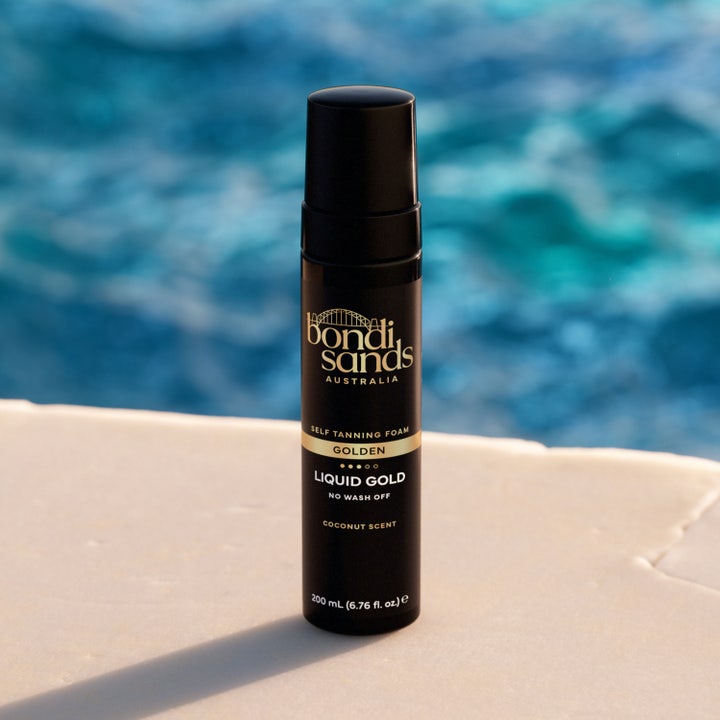 Bondi Sands Liquid Gold Self Tanning Foam 200 ml gir gyllen glød i svart pumpeflaske plassert ved et blått basseng.