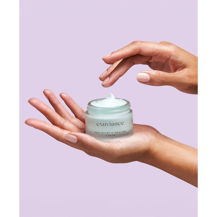 Exuviance Pro-Plump Hydrating Cream 45 g fuktighetsgivende nattkrem i frostet krukke med lyseblå krem holdt i en hånd
